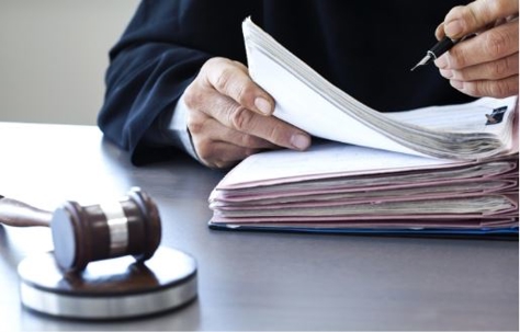 a person writing on a binder of documents and a judge's gavel on the table